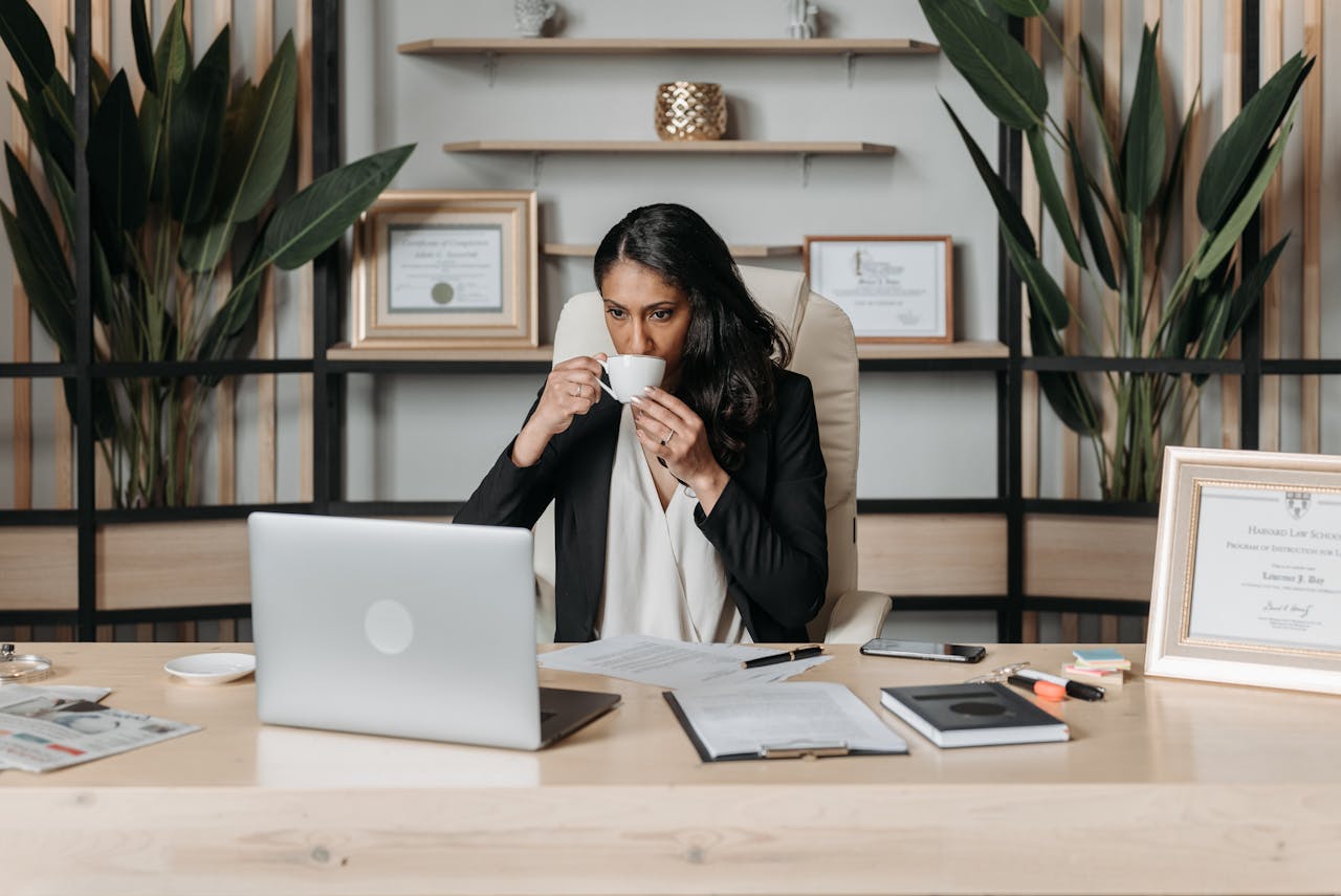 Lawyer sat a desk drinking a cup of coffee whilst working at a laptop.