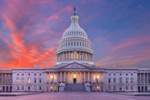 U.S. Capitol building at sunset with the dome illuminated against a vibrant sky.
