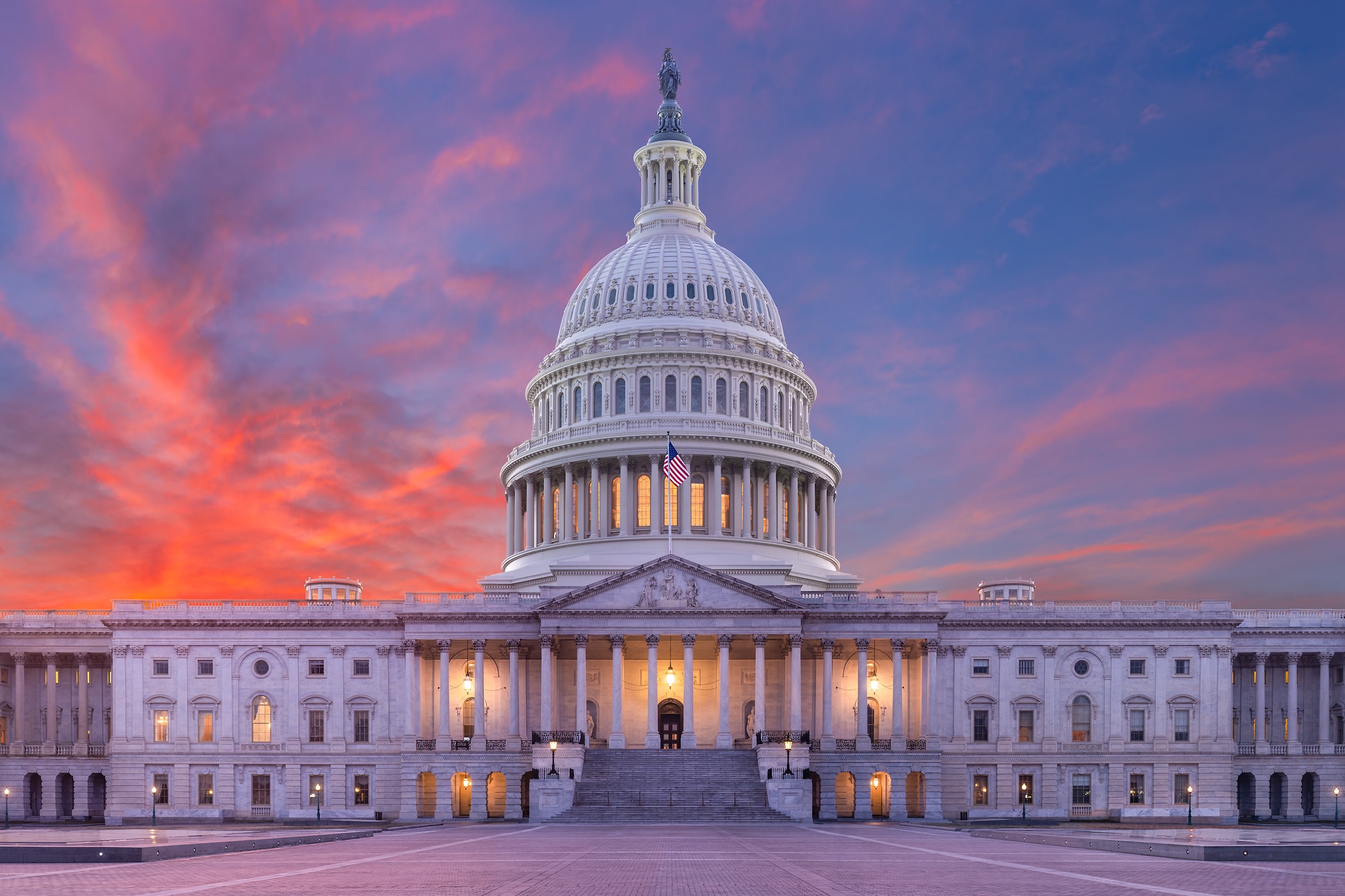 U.S. Capitol building at sunset with the dome illuminated against a vibrant sky.