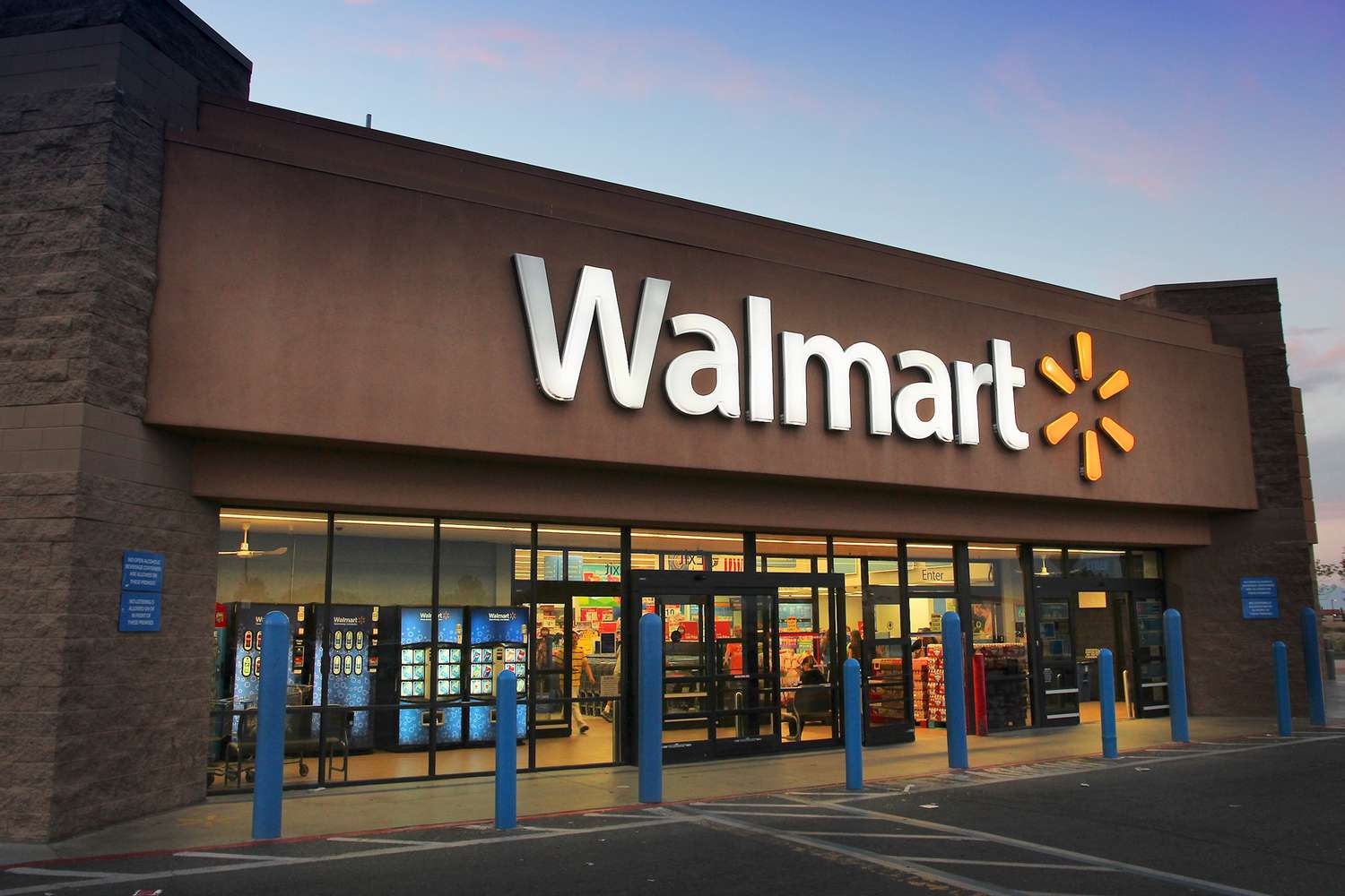 Exterior of a Walmart store at sunset with the illuminated Walmart logo above the entrance.
