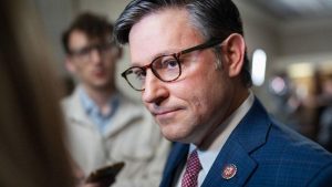 A U.S. representative, wearing a suit and congressional lapel pin, meets with reporters during discussions involving House Speaker matters.