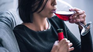 A person drinking a glass of red wine while holding a wine bottle.