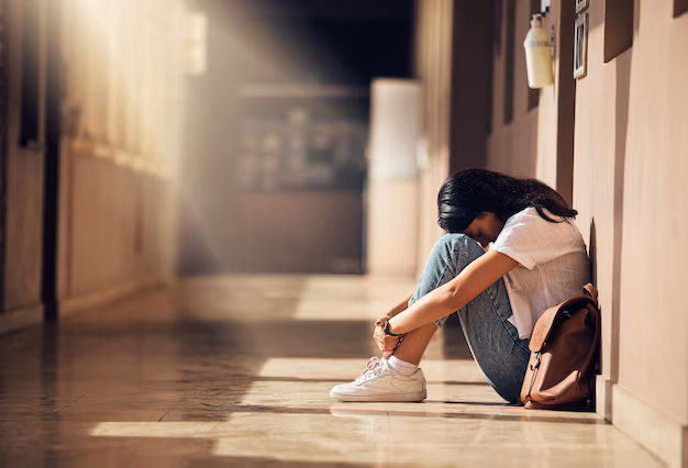 A teenager sits alone in a quiet school hallway, reflecting with their knees pulled close, symbolizing the hidden and isolating nature of teen dating violence.
