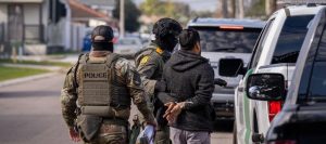 Federal agents detain a man during an immigration operation on a residential street.