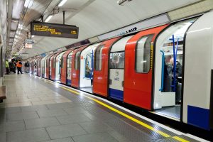 Passengers boarding a London Underground train at an open platform inside a tube station.
