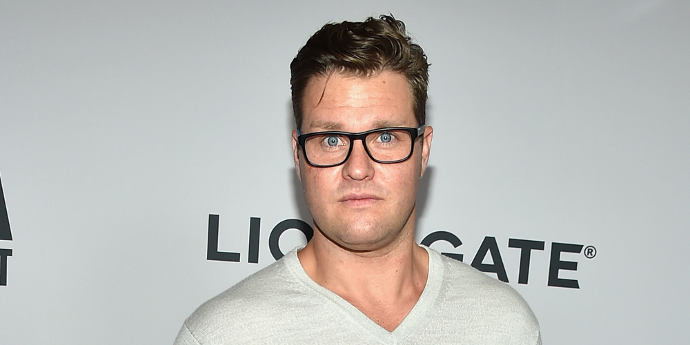 Zachery Ty Bryan attending a Lionsgate event, wearing glasses and a light grey shirt.