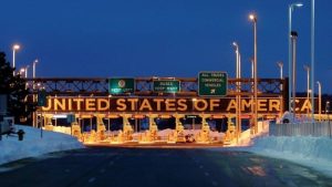Border toll plaza at night with &ldquo;United States of America&rdquo; sign illuminated overhead
