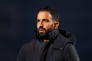 Manchester United head coach wearing a black padded jacket on the touchline during an evening match.