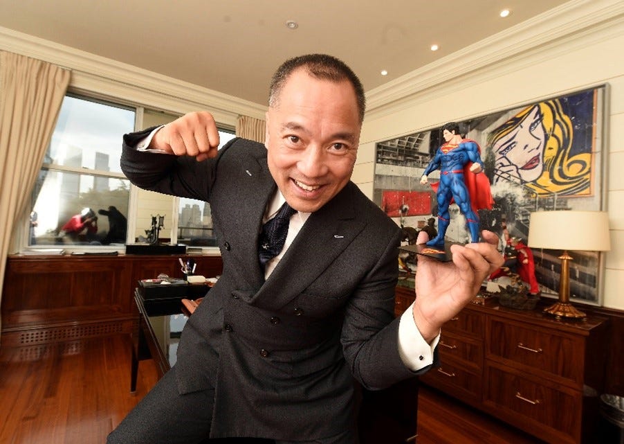 Miles Guo poses inside an office holding a Superman figurine