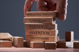man adding a block showing the words intellectual property on top of other wooden block with text copyright, patents, invention,and trademark